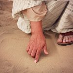 Scrive sulla sabbia con il dito